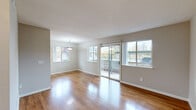 This single-floor, 2-bedroom, 1-bathroom residence offers a thoughtfully designed layout across a compact yet functional footprint. The living area is a bright, open space highlighted by gleaming hardwood floors, neutral-toned walls, and large windows that flood the room with natural light. A sliding glass door provides direct outdoor access and frames views of the surrounding neighborhood, while a pendant light fixture adds a subtle decorative touch. The galley-style kitchen is well-equipped, featuring white shaker cabinets, granite-look countertops, stainless steel appliances including a gas range and refrigerator, and hardwood flooring that continues from the main living area. A stainless steel sink with a window above completes the practical layout. Both bedrooms are carpeted for comfort and finished with neutral tones. The primary bedroom offers a generous footprint with mirrored sliding closet doors, while the second bedroom features a window with neighborhood views and its own closet. The full bathroom is clean and functional, with a tub-shower combination, hardwood flooring, and a vanity with granite-look countertops. A hallway and entrance area complete the efficient floor plan, connecting all rooms seamlessly throughout the home.