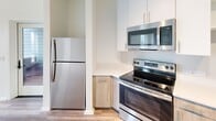 Located at 401 A St in Wilmington, Delaware, this modern single-floor unit offers four bedrooms and two bathrooms within a thoughtfully designed layout. The open living room is bathed in natural light through large windows framing views of the surrounding cityscape and nearby waterfront, complemented by smooth hardwood-style flooring throughout the main living areas.

The kitchen features stainless steel appliances, including a refrigerator, electric range, and over-the-range microwave, paired with light wood cabinetry, clean white countertops, an undermount sink, a dishwasher, and open shelving that adds a functional, contemporary touch.

The bedrooms are carpeted for comfort, with at least one room offering a dedicated closet with built-in shelving. One bedroom provides a striking waterfront view through a large picture window, making it a standout feature of the unit.

The two bathrooms are finished with neutral large-format tile flooring and matte black fixtures. One bathroom includes a tub-shower combination with vertical tile surround, while the other features a walk-in shower with a tiled base and grab bars.

A central hallway connects the rooms efficiently, with recessed lighting and wood-look flooring maintaining a cohesive, clean aesthetic throughout the entire space.
