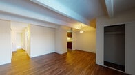 This single-floor unit is defined by a cohesive blend of practical design and comfortable living spaces. The main living area is a spacious, open room showcasing warm hardwood flooring that runs throughout much of the unit. A textured ceiling with distinctive exposed beams adds architectural character overhead, while a pendant light fixture provides focused illumination near the transition to the kitchen. A built-in closet with a sliding door offers convenient storage directly within the living space.

The kitchen is efficiently laid out with rich, dark wood cabinetry, granite-style countertops, and black appliances including a refrigerator, dishwasher, and range. The hardwood flooring continues into this area, maintaining visual continuity throughout.

The bedroom is carpeted, offering a softer underfoot experience, and receives natural light through a window fitted with vertical blinds. A baseboard heating unit runs along the wall, ensuring comfort year-round.

The bathroom features a wide vanity with a granite-style countertop, an undermount sink, dark wood cabinetry, and a large mirror with overhead lighting. A separate tiled wet area with a shower-tub combination is accessible through a dedicated doorway, completing the functional layout of this well-designed space.