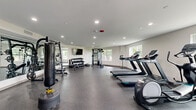 Located at 2305 Sokol Ct in Darien, IL, this dedicated fitness center offers a comprehensive exercise environment designed to support a wide range of workout routines. The single-floor space is thoughtfully laid out to maximize functionality and flow, with durable rubber flooring throughout that provides both safety and comfort during exercise.

The cardio zone features multiple treadmills and an elliptical machine, positioned near windows that allow natural light to fill the space and offer pleasant outdoor views of the surrounding greenery. A large standing fan provides additional air circulation in this area.

The strength training section is well-appointed with a multi-functional cable machine, a Smith machine with an adjustable bench, and a full rack of dumbbells organized on tiered storage. Full-length mirrors line one wall, enhancing the sense of space and allowing users to monitor their form during workouts. A wall-mounted flat-screen TV adds an entertainment element to the training environment.

Additional functional fitness equipment, including stability balls, medicine balls, and a punching bag, is available for varied training. Recessed lighting overhead ensures the space remains bright and well-illuminated at all times. Glass partition doors connect the fitness center to an adjacent lounge area, contributing to an open and accessible feel throughout the facility.