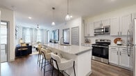 This single-floor residence showcases a thoughtfully designed open-concept layout that seamlessly connects the kitchen, dining, and living areas. The kitchen serves as a central hub, anchored by a generously sized island with a striking granite countertop, an undermount sink, and seating for multiple bar-height chairs. Pendant lighting illuminates the island from above, while white shaker-style cabinetry, a classic subway tile backsplash, and a full suite of stainless steel appliances — including a range, microwave, and refrigerator — complete the space. Dark-toned hardwood-style flooring flows throughout the main living areas, creating a warm contrast against the bright, neutral walls.

The living room offers a comfortable, well-proportioned space with a ceiling fan, natural light from multiple windows, and direct visual connectivity to the kitchen. Each bedroom features plush carpeting, ceiling fans, and windows that bring in natural light. The primary bathroom includes a granite-topped vanity with white cabinetry, a large mirror, and a glass-enclosed walk-in shower with tile surround. A dedicated in-unit laundry area with a full-size washer and dryer adds practical convenience throughout.