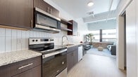 Located at East First Street North in downtown Wichita, Kansas, this single-floor unit offers a well-designed open layout that merges contemporary finishes with industrial-inspired character. Light wood-style flooring runs throughout, providing a cohesive foundation that connects each area of the space.

The kitchen is outfitted with dark espresso cabinetry, granite countertops, and a full suite of stainless steel appliances, including an electric range with over-the-range microwave, refrigerator, and dishwasher. A white subway tile backsplash adds a clean contrast to the rich cabinetry, while open shelving provides both function and visual interest. The kitchen flows directly into the living area, enhancing the open feel of the floor plan.

The living area is a standout feature, highlighted by an exposed red brick accent wall and expansive windows that invite generous natural light and urban views. The combination of raw brick and modern finishes creates a distinctive loft-inspired ambiance.

The bedroom is a calm, neutral retreat with light walls, continued wood-style flooring, and ample natural light. The bathroom features granite countertops, white cabinetry with brushed nickel hardware, and a clean, minimalist aesthetic consistent with the rest of the unit.