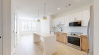 Located at 1610 N St Marys St in San Antonio, TX, this thoughtfully designed one-bedroom, one-bathroom residence offers a clean, modern aesthetic across its single floor. The open-concept layout seamlessly connects the kitchen and living area, creating an airy and functional living space bathed in natural light from large windows with blinds.

The kitchen is a standout feature, showcasing a two-tone design with crisp white upper cabinets and warm natural wood lower cabinets, all accented by matte black hardware. A large white waterfall-edge island serves as both a prep space and casual gathering spot, illuminated by stylish globe pendant lights with gold interiors. Stainless steel appliances, including a refrigerator, range, microwave, and dishwasher, complete the space alongside a sleek matte black faucet and white tile backsplash.

The bedroom offers a calm retreat with plush carpet flooring, a ceiling fan, and natural light. It includes access to a walk-in closet with built-in shelving. The bathroom features a floating white vanity, a large framed mirror, matte black fixtures, and light wood-tone flooring. Light wood floors run throughout the main living areas, tying the home's contemporary design together cohesively.