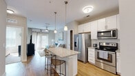 This single-floor residence offers a thoughtfully designed open-concept layout that seamlessly connects the kitchen, dining, and living areas. The kitchen serves as a central hub, showcasing white shaker-style cabinetry, granite countertops, and a full suite of stainless steel appliances including a French door refrigerator, electric range, built-in microwave, and dishwasher. A kitchen island with seating for two is accented by pendant lighting overhead, making it ideal for casual dining or entertaining. White subway tile backsplash adds a clean, classic touch throughout the kitchen.

Light wood-style flooring runs throughout the main living areas, contributing to a warm and cohesive aesthetic. The living room features a ceiling fan, large French doors that invite natural light, and an open connection to the rest of the space. The bedroom is carpeted for comfort and includes multiple windows with natural light, a ceiling fan, and ample space for furnishings.

The bathroom is well-appointed with an extended dual-sink vanity, wood-look tile flooring, a large mirror, and a glass-enclosed walk-in shower with neutral tile surround. Clean lines and neutral tones throughout create a calm, contemporary ambiance.
