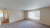 This single-floor unit offers a practical and well-organized layout across several distinct living areas. The living room is generously sized, featuring neutral-toned carpeting and a large picture window with vertical blinds that allows abundant natural light to fill the space. A ceiling fan overhead adds to the comfort of the open living and dining area, which flows toward the kitchen.

The galley-style kitchen is efficiently designed, featuring warm wood cabinetry on both sides, white appliances including a range, microwave, dishwasher, and refrigerator, and light-toned countertops. Vinyl tile flooring runs throughout the kitchen, providing a clean and durable surface.

The bedrooms are carpeted and well-lit, each featuring windows with blinds that offer views of the surrounding exterior. One bedroom includes access to a spacious walk-in closet equipped with a full-length hanging rod and shelving, offering generous storage capacity.

The bathroom is notably spacious, showcasing a dual-sink vanity with rich wood cabinetry, a large mirror, pendant lighting, and vinyl tile flooring. Additional storage space is visible throughout, including utility access with HVAC infrastructure. Overall, the unit presents a clean, neutral palette with functional finishes suited for everyday living.