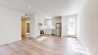 This well-designed single-floor residence offers a clean, modern aesthetic throughout, characterized by crisp white walls, recessed lighting, and an abundance of natural light. The open living area greets visitors with light-toned hardwood flooring and a striking navy pivot door that opens to an outdoor space, framing views of lush greenery. Windows fitted with horizontal blinds allow for adjustable natural light across the main living spaces.

The kitchen is thoughtfully appointed with white shaker cabinetry, a classic white subway tile backsplash, and a full suite of stainless steel appliances, including a refrigerator, range, microwave, and dishwasher. Light wood flooring continues seamlessly from the living area into the kitchen, reinforcing the open, airy feel of the shared spaces.

The bedrooms offer a comfortable retreat, with some featuring warm neutral carpet and others continuing the light hardwood flooring. Each room includes windows with exterior views and ample wall space for flexible arrangement.

The bathroom is a standout feature, showcasing bold geometric hexagonal floor tile in a black-and-white pattern, paired with a white vanity, clean countertops, and a well-lit mirror. The overall design of this residence balances contemporary finishes with a welcoming, functional layout.
