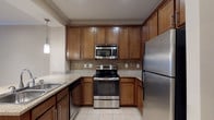 This single-floor residence at 3410 Alexander Rd in Atlanta, Georgia offers a thoughtfully designed layout with functional and comfortable living spaces throughout. The kitchen is a standout feature, outfitted with rich warm-toned cabinetry, granite countertops, a tile backsplash, and a full suite of stainless steel appliances including a refrigerator, electric range, over-the-range microwave, and dishwasher. Light tile flooring runs underfoot, and pendant lighting adds a refined touch above the breakfast bar that opens into the living area. The living space is generously proportioned, featuring soft neutral carpet, crown molding, a tray ceiling with a ceiling fan, and track lighting that illuminates the open-concept flow toward the kitchen. The bedroom offers plush carpeting, large windows with blinds that invite natural light, and a tray ceiling with track lighting, creating a bright and restful retreat. The bathroom is tastefully finished with tile flooring, a granite-topped vanity with wood cabinetry, and an arched alcove housing a full soaking tub with a tiled surround. Throughout the residence, neutral tones, clean lines, and quality finishes contribute to a cohesive and welcoming ambiance.