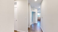 This single-story space presents a clean, contemporary design throughout. A central hallway with wood-look flooring and recessed lighting connects the various areas, creating a cohesive and functional flow. The hallway leads past multiple doorways, offering convenient access to each room.

The kitchen is a standout feature, showcasing a combination of white upper cabinetry and light wood lower cabinets paired with white quartz countertops and a white subway tile backsplash. Stainless steel appliances, including a range, built-in microwave, and dishwasher, complement the modern aesthetic. Natural light enters through a window above the sink, brightening the workspace.

The bedrooms feature plush carpeting and large windows dressed with horizontal blinds, providing ample natural light and outdoor views. Ceiling fans are present in multiple rooms, enhancing comfort. A spacious walk-in closet with built-in wire shelving and hanging rods offers generous storage capacity.

The bathroom is well-appointed with a light wood vanity, white quartz countertop, undermount sink, brushed nickel fixtures, a tiled tub-shower combination, and wood-look flooring, rounding out this thoughtfully designed space.