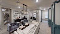 This single-floor amenity and co-working space is thoughtfully designed to support both focused work and collaborative gatherings. The layout flows seamlessly between distinct functional zones, each finished with a cohesive transitional design palette of neutral tones, soft carpeting, and warm metallic accents.

The central lounge area serves as the heart of the space, anchored by a plush white sofa and a pair of tufted gray velvet armchairs arranged around rustic wooden accent tables. An oversized industrial-style lantern pendant illuminates the area, while a bold typographic wall mural featuring an Arnold Palmer quote adds character and motivational energy to the room.

Adjacent to the lounge is a well-appointed coffee bar with dark cabinetry, a tile backsplash, and a coffee station, alongside a high-top counter with bar stools for informal seating.

A dedicated conference room features a long wooden table surrounded by upholstered office chairs, a mounted flat-screen display, a chandelier, and natural light from draped windows—ideal for meetings and presentations.

Private office pods with teal-trimmed French doors and shiplap-accented interiors provide individual workstations for focused tasks. A printer station and additional seating areas complete this well-rounded, professional environment.