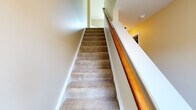 This three-story home is thoughtfully designed across multiple levels, offering a functional layout with a variety of living spaces. The main living area features plush wall-to-wall carpeting and a ceiling fan, opening directly to a kitchen pass-through that creates a seamless connection between rooms. The kitchen is well-equipped with warm oak cabinetry, stainless steel appliances including a range, microwave, refrigerator, and dishwasher, complemented by granite-look countertops and light hardwood flooring. A window provides natural light and outdoor views of the surrounding neighborhood. The upper level hosts carpeted bedrooms filled with natural light from standard windows, along with two bathrooms — one featuring a tub-shower combination and oak vanity, and another with a standalone shower stall, both finished with light hardwood flooring. Carpeted stairs with a warm oak handrail connect the floors, adding a classic touch to the vertical flow of the home. The lower level includes an attached garage with an automatic opener and a dedicated utility room housing a water heater and laundry hookups, with a concrete block foundation providing a sturdy, practical base for the home.