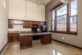 Located at 104 SW Fourth St in the heart of downtown Des Moines, Iowa, this loft-style unit offers a distinctive industrial aesthetic across a single floor. Soaring ceilings throughout create a dramatically open atmosphere, accentuated by exposed ductwork and structural elements that speak to the building's urban character. Polished concrete floors with warm, variegated tones run continuously throughout the space, lending a sleek yet raw quality underfoot.

The kitchen is a standout feature, equipped with rich dark wood cabinetry, granite-style countertops, and black appliances including a gas range, built-in microwave, and refrigerator. A peninsula island provides additional prep space and casual seating, while large windows frame views of the surrounding downtown skyline, flooding the area with natural light. Pendant lighting suspended from the high ceilings adds an inviting glow.

The living and bedroom areas are open and versatile, featuring dark wood door and window trim that contrasts smartly against the light walls. A closet with built-in shelving offers practical storage. The bathroom is clean and functional, featuring a full tub-shower combination, a wood-toned vanity, and consistent concrete flooring. A ceiling fan and accessible electrical panel complete the practical amenities of this urban downtown residence.
