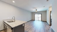 This single-floor residence at 115 SW Eagles Pkwy in Grain Valley, Missouri offers a thoughtfully designed open-concept layout with contemporary finishes throughout. Light-toned luxury vinyl plank flooring runs through the main living areas, creating a cohesive and clean aesthetic, while plush carpet adds comfort to the bedrooms.

The kitchen serves as a focal point of the living space, showcasing a bold navy-blue island with granite countertops and an integrated sink, contrasted by light gray shaker-style cabinetry and a classic white subway tile backsplash. Stainless steel appliances, including a refrigerator, range, and built-in microwave, complete the well-equipped cooking area. Recessed lighting and a ceiling fan keep the open living and dining area bright and comfortable, with sliding glass doors leading to a private balcony.

The bedrooms feature plush carpet, ceiling fans, and natural light from windowed walls with blinds. At least one bedroom includes access to a walk-in closet with built-in shelving, while another offers dual-door closet access. The bathroom is finished with granite-topped gray cabinetry, a full tub-shower combination, and warm vanity lighting, maintaining the modern aesthetic found throughout the space.