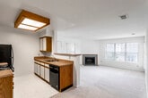 This single-floor unit is designed with a practical, open layout that connects the kitchen and living areas seamlessly. The kitchen is configured as a galley-style space, featuring oak-trimmed cabinetry, laminate countertops, and black appliances including an electric range, microwave, refrigerator, and dishwasher. Light tile flooring runs throughout the kitchen, while neutral-toned carpet extends into the adjoining living and bedroom areas.

The living room is spacious and bright, benefiting from a large picture window that brings in generous natural light. A tile-surround fireplace serves as a functional focal point along one wall. A secondary room, accessible from the living area, includes a ceiling fan and sliding glass door opening to a private balcony with outdoor views.

An additional carpeted room provides flexible use as a bedroom or den, featuring neutral walls and multiple electrical outlets. The bathroom includes a single-sink vanity with wood-trimmed cabinetry, a toilet, and a full tub and shower combination. Tile flooring and a ventilation unit complete the functional bathroom layout. Throughout the unit, the consistent neutral color palette and clean lines contribute to a bright, understated ambiance.