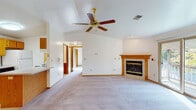 This single-floor home offers a well-organized layout with a warm, functional design throughout. The spacious living room immediately impresses with its vaulted ceiling, ceiling fan, and a wood-trimmed fireplace serving as a central focal point. A sliding glass door provides access to an outdoor deck and fills the room with natural light, while a decorative chandelier adds a finishing touch to the dining area nearby.

The kitchen features ample oak cabinetry extending to the ceiling, a double-basin sink, a peninsula with a breakfast bar, and tile flooring — providing generous storage and a practical workspace. The open connection between the kitchen and living/dining areas creates a cohesive, flowing common space.

The bedrooms are carpeted and well-lit by large windows that frame outdoor views of surrounding greenery. Each room benefits from ceiling fans for year-round comfort, and at least one bedroom includes a built-in closet with shelving for added storage.

The bathroom is equipped with a tub-shower combination, a single-basin vanity with a wide mirror, tile flooring, and oak-accented cabinetry and doors that carry through the home's consistent warm wood aesthetic. Throughout, neutral walls and light carpet tones create a clean, bright atmosphere ready to personalize.