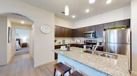 This single-story residence is thoughtfully designed with a modern aesthetic and cohesive finishes throughout. The open-concept kitchen serves as a central hub, showcasing dark espresso cabinetry, granite countertops, a subway tile backsplash, and a full suite of stainless steel appliances including a range, microwave, and refrigerator. A peninsula island with seating provides both additional prep space and a casual dining option, illuminated by pendant lighting overhead. Light wood-style flooring flows through the kitchen and main living areas, contributing to a clean, contemporary feel.

The living room is bright and inviting, featuring a sliding glass door that opens to an outdoor patio with exterior views, allowing natural light to fill the space. The layout connects seamlessly to the rest of the home through an arched entryway.

Multiple carpeted bedrooms offer comfortable retreats, each with closet space and room for generous furnishings. The primary bathroom features a dual-sink vanity with granite countertops, dark cabinetry, and a large mirror. A secondary bathroom includes a shower-tub combination, granite countertop vanity, and wood-style tile flooring, maintaining the consistent finish palette found throughout the home.