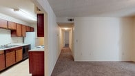 Located at 2908 Birmingham Hwy in Opelika, Alabama, this single-floor unit offers a practical and functional layout designed for comfortable everyday living. The open living area is finished with wall-to-wall carpet and neutral-toned walls, creating a clean, versatile space. A sliding glass door floods the room with natural light and provides access to a private balcony with outdoor views of surrounding greenery.

The galley-style kitchen is efficiently arranged with rich, dark wood cabinetry lining both walls, offering generous storage space. White appliances including an electric range, refrigerator, and dishwasher are provided, complemented by a double-basin sink and light-toned countertops. Light tile flooring runs throughout the kitchen area.

A central hallway connects the living space to the private rooms, with carpet continuing underfoot for a cohesive feel. The bathroom features light tile flooring, a wood-toned vanity with a single sink and mirror with strip lighting above, and a clean, all-white tub and shower combination with chrome fixtures. Textured ceilings are present throughout the unit. Central HVAC vents are visible in each room, ensuring year-round climate control. The overall layout is straightforward and well-suited for efficient, day-to-day use.