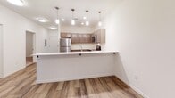 This single-floor residence at 565–603 First Ave NE in Faribault, Minnesota, offers a clean, modern aesthetic throughout its well-organized layout. The design emphasizes an open, functional flow between living and kitchen spaces, complemented by consistent neutral tones and contemporary finishes.

The kitchen serves as a standout feature, outfitted with taupe flat-front cabinetry, white countertops, and a full suite of stainless steel appliances, including a refrigerator, range, microwave, and dishwasher. Pendant lighting illuminates the workspace, and a peninsula with an extended countertop provides a convenient breakfast bar that opens toward the living area. Light wood-look flooring runs throughout the kitchen and main living spaces, contributing to a bright, cohesive feel.

The living area is generously proportioned, featuring the same wood-look flooring, a ceiling light fixture, and vertical blinds covering a sliding door or large window. The carpeted bedroom offers a quieter, softer environment with a window fitted with horizontal blinds that allows natural light to filter in.

The bathroom maintains the unit's modern style with tile flooring in a natural stone pattern, a vanity with matching cabinetry, and clean white walls accented by brushed nickel hardware. Overall, the space presents a well-appointed, move-in-ready environment with consistent modern detailing throughout.