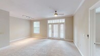 This single-story, 3-bedroom, 2-bathroom residence offers a thoughtfully designed floor plan that maximizes both comfort and functionality. The open living area is a standout feature, showcasing soft neutral tones, plush wall-to-wall carpeting, and crown molding that adds a refined architectural touch. A ceiling fan with light fixture keeps the space comfortable, while a set of French doors flanked by transom windows floods the room with natural light and provides direct access to an outdoor area. Track lighting adds additional illumination options. The kitchen is equipped with dark cabinetry and modern appliances, flowing seamlessly into the main living space as seen in the floor plan. The three bedrooms are finished in the same warm, neutral palette with plush carpeting throughout. The primary bedroom benefits from corner windows on two walls, offering abundant natural light and pleasant outdoor views of surrounding greenery. The secondary bedrooms are well-proportioned with natural light from individual windows. A dedicated laundry room houses a full-size front-loading washer and dryer set alongside a water heater, adding practical convenience. Clean white trim and baseboards throughout the residence contribute to a cohesive and polished aesthetic.