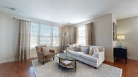 This single-floor residence offers a thoughtfully designed open-concept layout where the kitchen, dining, and living areas flow seamlessly together. Rich hardwood flooring runs throughout the main living spaces, anchoring the warm, neutral color palette. The living room is brightened by multiple windows dressed with elegant patterned drapes and horizontal blinds, allowing abundant natural light while offering privacy. A private door in the living area provides direct outdoor access.

The kitchen is a functional centerpiece, featuring dark espresso cabinetry, granite countertops, stainless steel appliances, and a white subway tile backsplash. A peninsula with bar seating and pendant lighting above serves as both a prep space and casual dining area, complemented by a dedicated dining space nearby.

The primary bedroom is a serene retreat with soft neutral tones, carpeted flooring, and ample space. A second bedroom features a distinctive olive-toned accent wall paired with coordinating artwork. Two bathrooms serve the residence: one with a soaking tub and dark vanity with granite counters, and another featuring a glass-enclosed walk-in shower with matching finishes, both finished with neutral tile flooring.