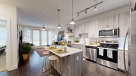 This well-designed single-floor residence offers a seamless open-concept layout that connects the kitchen, dining, and living areas into one cohesive living space. The kitchen is a standout feature, equipped with a full suite of stainless steel appliances including a refrigerator with ice maker, electric range, built-in microwave, and dishwasher. Light wood-toned cabinetry extends to the ceiling, providing generous storage, while quartz countertops and a subway tile backsplash add a clean, modern aesthetic. A central island with bar seating serves as both a prep area and casual dining spot, illuminated by stylish pendant lighting and a track lighting system overhead. Dark hardwood-style flooring runs throughout the main living areas, grounding the space with warmth and continuity. The living room is bright and inviting, benefiting from large French doors that allow abundant natural light and provide access to a private balcony. A ceiling fan adds to the comfort of the space. The bedroom is a peaceful retreat, featuring plush carpeting, a large window with sheer curtains, a ceiling fan, and a walk-in closet with built-in shelving. The bathroom is clean and functional, featuring a full tub-shower combination with white tile surround and neutral tile flooring.