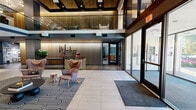 Located in the Central West End neighborhood of St. Louis, Missouri, Marlowe presents a thoughtfully designed common area that blends contemporary aesthetics with warm, inviting details. The grand lobby makes an immediate impression with its soaring double-height ceiling, slatted wood accent wall, and a striking branded reception desk accented with a bold geometric pattern. Large floor-to-ceiling glass entry doors flood the space with natural light, while a sculptural chandelier of clustered globe lights adds drama overhead.

The main lounge area features a sweeping curved sectional sofa and retro-inspired armchairs arranged atop a bold black-and-white graphic area rug, creating a comfortable yet visually dynamic gathering space. A mezzanine level overlooks the lobby below, offering additional seating with views into the heart of the space.

A dedicated lounge room provides a more intimate retreat, complete with floor-to-ceiling built-in wood shelving, a wall-mounted television, lush indoor planters, and flexible seating including a sunken bench area framed by a terracotta drapery panel. Nearby, a dining area features botanical wallcovering and a statement table with bold turned legs. A compact service nook with dark cabinetry, green subway tile, and neon signage rounds out the amenity offerings, delivering a cohesive and memorable residential experience.