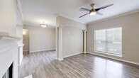 This thoughtfully designed single-floor residence offers a cohesive layout across one bedroom, one bathroom, a living room, dining room, kitchen, and a dedicated closet. The open living and dining area is an immediate standout, featuring elegant decorative columns with an arched detail that define the space without sacrificing openness. Light wood-tone flooring flows throughout, complemented by neutral warm-beige walls and crown molding that add a refined touch. A ceiling fan with a brushed bronze finish enhances the living area, while a fireplace adds warmth and character. Natural light enters through blinds-fitted windows, lending a bright and airy feel. The kitchen is well-equipped with stainless steel appliances — including a refrigerator, range, and microwave — set against crisp white cabinetry and a clean white countertop peninsula with an integrated sink, ideal for everyday cooking and casual dining. The bedroom is carpeted for comfort, features crown molding, a ceiling fan, and a window with outdoor views. Its walk-in closet provides generous storage with wire shelving and hanging rods on multiple walls. The bathroom offers a white vanity with brushed nickel hardware, a large mirror, and a tiled shower-tub combination, all finished with matching wood-tone flooring.