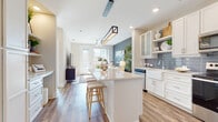 Located at 600 Calvert St in Charlotte, NC, this single-floor residence offers a thoughtfully designed open-concept layout with modern finishes throughout. The kitchen is a standout feature, anchored by a large central island with quartz countertops and bar seating, white shaker cabinetry, open shelving, a classic farmhouse sink with a subway tile backsplash, and stainless steel appliances—all complemented by warm hardwood-style flooring that flows seamlessly into the living area. The living room is bright and inviting, featuring a bold slate-blue accent wall, abundant natural light from large windows and a glass-paneled door, and a stylish ceiling fan overhead. The primary bedroom is serene and well-proportioned, bathed in natural light, with neutral tones that create a calm retreat. The en-suite bathroom is elegantly appointed with dual slate-blue vanities, granite countertops, large-format marble-look tile flooring, and a glass-enclosed walk-in shower. A second bedroom offers generous window views of the surrounding greenery, providing a bright and airy atmosphere. A dedicated built-in workspace area adds functional versatility to this well-rounded home.