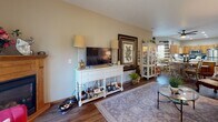 This single-floor home offers a thoughtfully designed open-concept layout that seamlessly connects the kitchen, dining, and living areas. The kitchen is equipped with warm oak cabinetry, a central island with a stainless steel dishwasher, and a full suite of stainless steel appliances including a refrigerator, range, and over-the-range microwave. A double-basin sink sits beneath a window, providing natural light throughout the workspace. Light wood-look flooring flows throughout the main living areas, lending a cohesive and airy feel to the home. The living room is a welcoming retreat, anchored by a gas fireplace with a wood mantel and sliding glass doors that open to the outdoors, filling the room with natural light and outdoor views. Recessed lighting and a ceiling fan add both functionality and style. Two bedrooms offer comfortable accommodations, each with closet space and warm, neutral tones. The primary bedroom features soft lavender walls and a built-in closet, while the second bedroom showcases classic charm. A full bathroom includes a single-vanity with oak cabinetry and a tub-shower combination. A dedicated laundry room with side-by-side washer and dryer and overhead oak cabinetry completes this practical and inviting home.