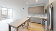 This single-floor unit at 3348 W Moore St in Richmond, Virginia, presents a clean, contemporary design with a cohesive aesthetic carried throughout every room. Light hardwood flooring runs continuously across the space, contributing to a bright, open atmosphere that is further enhanced by crisp white walls and modern trim details.

The kitchen is a standout feature, outfitted with two-tone cabinetry—combining warm taupe upper cabinets with sleek grey lower units—complemented by white quartz countertops, a subway tile backsplash, and a full suite of stainless steel appliances including a gas range, microwave, refrigerator, and dishwasher. A built-in island provides additional prep and dining space.

The living area benefits from large floor-to-ceiling windows and glass doors that flood the room with natural light and offer views of the surrounding neighborhood. The bedrooms are well-proportioned, with one featuring direct outdoor access via a large window wall, and another offering dual closets for ample storage. A walk-in closet is also present in one bedroom, accessible alongside an en-suite bath.

The unit includes two bathrooms: one with a soaking tub and tiled surround, and another with a glass-enclosed walk-in shower. Both are finished in a minimalist style consistent with the rest of the unit's modern character.