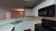 Located at 7827 Jefferson Place Cir in Baton Rouge, Louisiana, this single-floor residence offers a well-organized layout with a cohesive, neutral color palette throughout. The kitchen is equipped with white shaker-style cabinetry, light-toned countertops, a classic subway tile backsplash, and black appliances including an electric range and over-the-range microwave. A double-basin sink and ample counter space add to its functional appeal. The kitchen flows into a dedicated dining area, distinguished by rich dark hardwood-style flooring and an elegant chandelier that adds a refined touch. The open living area transitions seamlessly from the kitchen via a raised bar counter, featuring a ceiling fan with light fixture and a mix of dark hardwood-style flooring and plush carpeting. Carpeted bedrooms offer a comfortable retreat, each with ceiling fans and natural light provided by window treatments. Two full bathrooms are finished with white vanities, stone-patterned countertops, and tub-shower combinations. One bathroom features dark hardwood-style flooring for added contrast. Textured ceilings and warm taupe wall tones carry consistently throughout, giving the entire space a unified and welcoming ambiance.