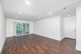 Located at 16550 Vanowen St in Los Angeles, CA, this 2-bedroom, 1-bathroom residence offers a thoughtfully designed single-floor layout. Rich hardwood-style flooring flows consistently throughout the home, complemented by crisp white walls and recessed lighting that create a bright, clean aesthetic.

The living room is an open, airy space bathed in natural light from a sliding glass door that leads to an outdoor balcony area, offering pleasant views of surrounding greenery. Recessed ceiling lights provide even illumination throughout the room.

The galley-style kitchen is well-appointed with white shaker cabinetry, gray countertops, a white subway tile backsplash, and stainless steel appliances including a gas range, microwave, and dishwasher. A window above the exterior door brings in additional natural light.

The primary bedroom is a comfortable, well-proportioned room featuring its own sliding glass door that opens directly to a private outdoor patio area, along with built-in upper cabinetry for added storage.

The bathroom is finished with large-format neutral tile and includes a glass-enclosed walk-in shower with a handheld showerhead and integrated niche shelving — a sleek, modern design.

A hallway connects the rooms efficiently, completing this well-organized and move-in-ready home.