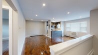 This thoughtfully updated single-floor unit offers a clean, modern aesthetic throughout. Polished hardwood floors run continuously across the living, dining, and bedroom areas, reflecting natural light and lending warmth to the neutral gray palette on the walls. The open-concept layout connects the living area seamlessly to the kitchen, which features a peninsula with a sleek white countertop and a contemporary dark blue base, dark-toned shaker cabinetry, a full suite of stainless steel appliances including a gas range, microwave, and refrigerator, and stylish pendant lighting overhead. Recessed lighting illuminates the living space, which also benefits from a large window fitted with white blinds. The bedrooms are generously proportioned, each with gleaming hardwood floors, wall-unit air conditioning, baseboard heating, and ample natural light. One bedroom includes a built-in closet with shelving. The bathroom is a standout feature, showcasing floor-to-ceiling marble-look porcelain tile surrounding a soaking tub, accented by a built-in niche and modern chrome fixtures. Throughout the unit, clean white trim, recessed lighting, and a consistent neutral color scheme create a cohesive and inviting atmosphere.