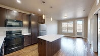 Located in Golden, Colorado, this one-bedroom, one-bathroom residence offers a well-designed single-floor layout that maximizes both function and comfort. The open-concept kitchen is a standout feature, showcasing rich dark-wood cabinetry extending to the ceiling, a white quartz-topped center island with pendant lighting, a white tile backsplash, and a full suite of stainless steel and black appliances including a refrigerator, range, microwave, and dishwasher. Hardwood-style flooring flows seamlessly through the kitchen and into the adjacent living area, which benefits from a large window and a glass-panel door leading to an outdoor balcony with scenic Colorado views. The bedroom is carpeted and well-proportioned, featuring a window that brings in natural light and views of the surrounding landscape, along with access to two closets for ample storage. The bathroom is finished with large-format light tile flooring, a clean white vanity with dark wood accents, and a full tub-shower combination. A stacked washer and dryer unit is also included within the unit, adding everyday convenience to this efficiently planned Golden, CO residence.