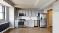 Located at 50 W Broad St in the heart of downtown Columbus, Ohio, this single-floor unit offers a thoughtfully designed layout with contemporary finishes throughout. The open-concept living area is anchored by warm hardwood flooring, neutral-toned walls, and architectural ceiling details that add visual interest. Multiple windows allow natural light to fill the space, with views of the surrounding urban environment.

The kitchen is outfitted with gray shaker-style cabinetry, white countertops, a classic subway tile backsplash, and a full suite of stainless steel appliances, including a gas range, built-in microwave, dishwasher, and a French door refrigerator with an in-door water and ice dispenser. The kitchen flows seamlessly into the living area, making it well-suited for daily living and entertaining.

The bedroom features plush wall-to-wall carpeting, a sizable window with natural light, and access to a closet. The bathroom is finished with marble-style tile on both the floors and shower surround, complemented by a glass-enclosed tub-shower combination and a single-sink vanity with ample storage beneath. The overall aesthetic throughout the unit is clean, modern, and move-in ready.