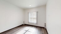 This single-floor residence offers a thoughtfully planned layout with three bedrooms, two bathrooms, a kitchen, two closets, and a hallway connecting the living spaces. The interior features hardwood-style flooring throughout, complemented by crisp white walls and dark baseboards that create a clean, modern aesthetic.

The kitchen is a functional highlight, featuring contemporary grey cabinetry with sleek hardware, white appliances including a range and refrigerator, and a peninsula with a light-toned countertop that provides additional workspace and seating. Recessed lighting illuminates the space effectively.

The bedrooms are bright and well-proportioned. The generously sized primary bedroom benefits from natural light through a window fitted with vertical blinds, and includes access to a dedicated closet with built-in shelving. The secondary bedrooms are similarly designed, each offering hardwood-style flooring and natural light from exterior-facing windows.

The two bathrooms are finished in a clean, minimalist style. One features a single-sink vanity with grey cabinetry and a mirror above, while the other includes a full bathtub-shower combination with white tile surround. Both bathrooms feature hardwood-style flooring and bright, neutral finishes that maintain a consistent modern character throughout the residence.