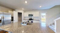 Located in Bolivia, NC, this two-story home offers a well-designed layout spread across two floors. The main level features an open-concept living room and kitchen, both finished with warm wood-look luxury vinyl plank flooring. The living room is fitted with a ceiling fan and receives natural light through a front-facing window. The kitchen is a standout space, showcasing granite countertops, white shaker-style cabinetry, stainless steel appliances including a range and microwave, a large island with a built-in sink, and a spacious walk-in pantry with wire shelving. A door from the kitchen provides direct access to the exterior. The main floor also includes an attached garage equipped with an automatic opener and an electrical panel. Upstairs, three bedrooms are finished with plush carpet and ceiling fans, each with windows offering neighborhood views. The generously sized primary bedroom includes a dedicated closet with wire shelving. Three full bathrooms are distributed throughout the home, with at least one featuring a tub-shower combination. A hallway connects the upper-level rooms, completing this clean, move-in-ready home.