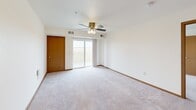 Located at 830 Roberts Rd in Sartell, Minnesota, this single-floor unit offers a functional and well-organized layout across several distinct living areas. The kitchen is equipped with warm medium-toned wood cabinetry, recessed lighting, a breakfast bar peninsula with a built-in sink, and black appliances including a range and refrigerator. Light hardwood-style flooring runs through the kitchen and connects seamlessly to surrounding areas.

The living room is spacious and carpeted, featuring a ceiling fan, sliding glass door access to a private balcony, and open sightlines toward the kitchen. An adjacent area with matching carpet provides flexible use as a dining or secondary living space. Bedrooms are carpeted and well-sized, with windows offering open views of the surrounding landscape. Closets with rod storage are present in the bedrooms.

Two full bathrooms feature matching warm wood vanities with white countertops, tub-shower combinations, and stone-tile flooring, providing a cohesive aesthetic throughout. A dedicated laundry room with hardwood-style flooring accommodates a full-size washer and dryer with overhead shelving. The overall interior maintains a clean, neutral palette with warm wood trim accents throughout.