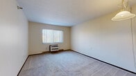 Located at 1356 Athena Lane in Zanesville, Ohio, this one-bedroom, one-bathroom unit offers a practical and efficient single-floor layout. The living room is a comfortable, open space featuring wall-to-wall carpeting, neutral-toned walls, a textured ceiling, and a large window dressed with vertical blinds that invites natural light and outdoor views. A wall-mounted HVAC unit provides climate control, and a pendant light fixture adds a functional accent overhead. The kitchen is positioned adjacent to the living area and is equipped with a double basin sink, warm wood-toned cabinetry, and light countertops, offering a convenient and organized workspace. The bedroom is a well-proportioned, carpeted room with its own window overlooking the outdoors and a baseboard heating unit along the wall. A sliding wood-panel closet door provides generous built-in storage with a full-width hanging rod. The bathroom features a clean, white tub and shower combination with safety grab bars, tile flooring, and essential fixtures. Three closets throughout the unit offer ample additional storage. The hallway connects the rooms efficiently, contributing to the unit's straightforward and accessible flow.