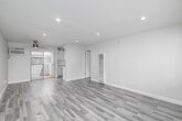 Located at 9999 Imperial Hwy in Downey, CA, this single-floor residential unit offers a thoughtfully designed layout comprising a combined kitchen and living room, one bedroom, and a hallway. The interior is finished in a clean, modern aesthetic with light gray wood-style flooring running throughout all rooms, complemented by crisp white walls and bright recessed lighting.

The open living area is generously proportioned, featuring a ceiling fan, a wall-mounted A/C unit, and a sliding glass door that opens to a balcony, filling the space with natural light. A large window in the living room further enhances the bright, airy atmosphere.

The kitchen is well-appointed with white shaker-style cabinetry, sleek silver bar-pull hardware, white quartz countertops, and a decorative penny-tile backsplash. Stainless steel appliances include a gas range, over-the-range microwave, dishwasher, and refrigerator, making it both functional and stylish.

The spacious bedroom is a comfortable retreat, offering a ceiling fan, a wide window with outdoor views of the surrounding neighborhood, and a mirrored sliding-door closet that adds both storage and visual depth to the room. The hallway connects the living spaces efficiently, completing this well-designed unit.