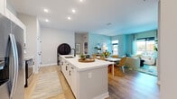 Located at 795 Ironwood Flats Cir in Brandon, FL, this single-floor residence offers a thoughtfully designed open-concept layout with a cohesive coastal color palette of soft teals, blues, and crisp whites. The kitchen serves as a central hub, featuring a large island with a white quartz countertop, an undermount sink with a matte black faucet, white shaker cabinetry, stainless steel appliances, and a subway tile backsplash. Bar seating along the island connects seamlessly to the adjacent dining and living areas, which are bathed in natural light from large windows overlooking outdoor views. Light wood-look flooring flows throughout the main living spaces, enhancing the bright and airy feel. The living room offers generous proportions with ample natural light and direct access to an outdoor patio area. The primary bedroom features a striking full-wall watercolor mural as a headboard accent, plush carpeting, and an outdoor view. Its en-suite bathroom includes a double-sink vanity with white cabinetry and matte black hardware, a glass-enclosed walk-in shower, a walk-in closet, and light wood-look tile flooring. The secondary bedroom also enjoys natural light and outdoor views, while the secondary bathroom is finished with white cabinetry, matte black fixtures, and a shower-tub combination.