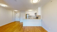 This well-designed two-bedroom, one-bathroom unit makes efficient use of its compact footprint across a single floor. The open-concept living and kitchen area serves as the heart of the space, where a peninsula with a light stone countertop separates the kitchen from the living area. The kitchen is outfitted with high-gloss white cabinetry, a subtle tile backsplash, and a full suite of stainless steel appliances including a range, microwave, and refrigerator. Warm hardwood-style flooring flows consistently throughout the entire unit, lending cohesion and brightness to every room.

Both bedrooms are well-proportioned and benefit from large windows that allow generous natural light and urban views of the surrounding cityscape. A sliding glass door in the primary bedroom opens to a balcony, extending the living space outdoors. Each bedroom includes a built-in closet with shelving and hanging rods for organized storage. The second bedroom also features a built-in closet and a bright window with a baseboard heater beneath it.

The bathroom features a combined tub and shower, a white vanity with a stone countertop, and hardwood-style flooring. The unit's clean, neutral palette and modern finishes create a bright, functional living environment throughout.
