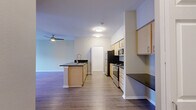 Located at 1617 E Main Ave in Puyallup, Washington, this single-floor unit offers a clean, modern aesthetic with a thoughtfully designed open-concept layout. The kitchen is a standout feature, equipped with stainless steel appliances including a refrigerator, range, and built-in microwave. Light maple cabinetry pairs with dark granite-style countertops to create a striking contrast, while a central island with a deep sink and matching countertop adds both prep space and a natural divide between the kitchen and living area. A built-in countertop nook along one wall provides additional workspace or storage. The living area is generously proportioned, featuring wood-look luxury vinyl plank flooring that extends seamlessly throughout the unit, lending warmth and continuity. A ceiling fan with a light fixture keeps the space comfortable year-round. Neutral, light-toned walls create a bright and airy ambiance, while a sliding glass door in the living area introduces natural light and provides access to the outdoors. Additional rooms offer flexible space with clean lines, crisp white trim, and the same durable flooring, making them well-suited for a variety of uses. The overall design is contemporary and functional, ideal for comfortable everyday living.