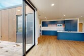 Located at 275 Pendleton Way in Washougal, Washington, this thoughtfully designed single-floor residence offers a clean, contemporary aesthetic throughout. Light wood-tone flooring runs consistently across the space, complementing the bright white walls and recessed lighting that keep the interior feeling open and airy.

The kitchen is a standout centerpiece, outfitted with bold navy-blue cabinetry that extends floor to ceiling, open wood-accent shelving, a white tile backsplash, built-in appliances including a microwave and oven, and a matching navy island with a white countertop and integrated sink. In-unit laundry is conveniently tucked nearby.

The living area benefits from an expansive wall of black-framed floor-to-ceiling windows that flood the space with natural light and frame sweeping views of the surrounding mountains and Washougal cityscape. A sliding glass door leads directly to a wood-deck outdoor terrace, extending the living space outdoors. Individual rooms also feature large windows and wall-mounted mini-split HVAC units.

The bathroom is finished with classic penny-tile flooring, a floating navy vanity with a white countertop, a round mirror with a black frame, and refined gold accent hardware. Throughout the unit, black hardware details provide a cohesive modern touch, resulting in a polished and well-curated living environment.