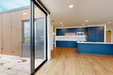 Located at 275 Pendleton Way in Washougal, Washington, this thoughtfully designed single-floor residence offers a clean, contemporary aesthetic throughout. Light wood-tone flooring runs consistently across the space, complementing the bright white walls and recessed lighting that keep the interior feeling open and airy.

The kitchen is a standout centerpiece, outfitted with bold navy-blue cabinetry that extends floor to ceiling, open wood-accent shelving, a white tile backsplash, built-in appliances including a microwave and oven, and a matching navy island with a white countertop and integrated sink. In-unit laundry is conveniently tucked nearby.

The living area benefits from an expansive wall of black-framed floor-to-ceiling windows that flood the space with natural light and frame sweeping views of the surrounding mountains and Washougal cityscape. A sliding glass door leads directly to a wood-deck outdoor terrace, extending the living space outdoors. Individual rooms also feature large windows and wall-mounted mini-split HVAC units.

The bathroom is finished with classic penny-tile flooring, a floating navy vanity with a white countertop, a round mirror with a black frame, and refined gold accent hardware. Throughout the unit, black hardware details provide a cohesive modern touch, resulting in a polished and well-curated living environment.