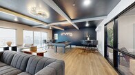 Located at 3911 20th Ave S in Fargo, North Dakota, this thoughtfully designed community lounge offers a sophisticated and inviting atmosphere across a single open floor. The space is defined by a striking contrast of dark navy and crisp white tones, with coffered ceilings painted in deep charcoal accented by white beams and an eye-catching starburst chandelier that adds a touch of modern elegance.

The lounge is organized into several distinct zones that flow seamlessly into one another. A game area anchors one side of the space, featuring a full-size pool table beneath an artistic neon light installation and a dark accent wall, accompanied by bar-height tables and sleek chairs for spectators. Adjacent to this is a cozy media and lounge area with a wall-mounted fireplace, flat-screen TV, and modular sectional sofas arranged for comfortable gathering.

Toward the exterior wall, oversized sliding glass windows flood the lounge with natural light and frame panoramic views of the Fargo skyline and surrounding landscape. A relaxed seating nook with plush neutral armchairs and a soft area rug creates a quieter retreat within the space. Light wood-tone flooring runs throughout, enhancing the warm yet contemporary feel. A glass-walled private room offers additional flexible space for meetings or smaller gatherings, completing this well-appointed lounge.