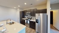 This single-story residence offers a thoughtfully designed open-concept layout that seamlessly connects the kitchen and living areas. The kitchen is a standout feature, showcasing rich dark espresso cabinetry that reaches toward the ceiling, a mosaic tile backsplash, light quartz countertops, and a full suite of stainless steel appliances including a refrigerator with ice maker, electric range, and built-in microwave. A kitchen island with matching countertops provides additional workspace and casual seating. Wood-look plank flooring runs throughout the kitchen and main living areas, transitioning to plush carpet in the living room and bedrooms.

The living area benefits from a ceiling fan and a tray ceiling detail that adds architectural interest. Bedrooms are generously proportioned, carpeted for comfort, and feature ceiling fans, neutral-toned walls, and windows that allow natural light. The primary bathroom is finished with dark cabinetry, a dual-sink vanity with quartz countertops, brushed nickel fixtures, large mirrors, and a tub-shower combination. A dedicated laundry room accommodates a full-size side-by-side washer and dryer with overhead shelving. Throughout the space, neutral warm-gray walls and consistent finishes create a cohesive, modern aesthetic.