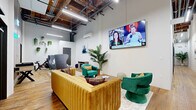 Located at 801 Broadway Blvd in the heart of Kansas City, MO, this single-floor lobby lounge seamlessly blends industrial character with modern, curated design. Soaring ceilings with exposed wood beams, open ductwork, and suspended linear lighting create a loft-like atmosphere that feels both expansive and welcoming. Rich hardwood floors run throughout, grounding the space with warmth and continuity.

The main lounge area serves as the visual centerpiece, anchored by a tufted golden velvet sofa paired with jewel-toned emerald green swivel chairs and a sculptural ridged wood coffee table atop a layered area rug. A wall-mounted flat-screen TV and curated artwork — including a large framed black-and-white figurative piece — add sophisticated visual interest. Lush tropical potted plants introduce natural vitality throughout.

A secondary seating nook features a cozy electric fireplace, marble-top nesting tables, navy velvet ottomans, and original artwork, offering an intimate retreat within the open layout. A neon "KC" sign and glowing wall accent add a playful local touch. Practical amenities include a bank of resident mailboxes and clearly marked access doors. The space is climate-controlled with a wall-mounted mini-split unit, ensuring year-round comfort in this thoughtfully appointed urban lounge.