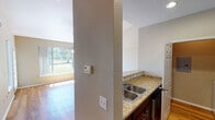 This single-floor residence offers a well-designed layout with consistent warm-toned hardwood flooring flowing throughout the main living areas and bedrooms. The main living space is bright and inviting, highlighted by vaulted ceilings, a ceiling fan, and a large picture window that frames lush outdoor greenery, flooding the room with natural light. An adjacent dining or flex area continues the open feel, also benefiting from abundant windows and direct access to an outdoor space via a glass-paneled door.

The kitchen is appointed with rich, dark cabinetry, granite countertops with warm undertones, a stainless steel double-basin sink, and stainless steel appliances including a GE range and over-the-range microwave. A structural column separates the kitchen from the main living area, adding architectural character to the open-concept flow.

The bedrooms are generously sized with hardwood floors, neutral wall tones, and closet access. One bedroom features a large sliding window overlooking a private balcony or patio area, providing an airy, connected feel to the outdoors. The bathroom includes a full tub and shower combination with clean white tile surround and chrome fixtures, offering a functional and tidy finish throughout.
