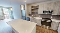 This contemporary 960 square foot apartment in Herndon, VA offers a well-designed living space with two bedrooms and two bathrooms. The open-concept floor plan seamlessly integrates the kitchen, living, and dining areas, creating a spacious feel. The kitchen boasts modern light wood cabinetry, stainless steel appliances, and a stylish brown subway tile backsplash. A large island with a quartz countertop provides additional workspace and casual seating.

The primary bedroom, measuring 140 square feet, offers ample space and includes a walk-in closet with custom shelving. Both bathrooms feature sleek finishes, including white tile flooring, wood vanities, and large mirrors. The apartment's neutral color palette and wood-look flooring throughout contribute to its modern aesthetic.

Large windows and a balcony door in the living area allow natural light to flood the space, while offering views of the surrounding area. The balcony provides an outdoor extension of the living space. Two closets in the unit offer additional storage options. Overall, this apartment combines contemporary design with practical amenities, creating an attractive and functional living environment.