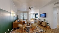 This well-appointed 2-bedroom, 2-bathroom single-story home offers a thoughtfully designed open-concept layout that seamlessly connects the living, dining, and kitchen areas. The bright living room features crown molding, a ceiling fan, hardwood-style flooring, and large windows that invite abundant natural light. Bold accent walls in deep teal and forest green add a distinctive, modern character throughout the space. The kitchen is a standout, outfitted with stainless steel appliances, white cabinetry, a sleek quartz countertop, and a breakfast bar with wood barstool seating — ideal for casual dining or entertaining. The adjacent dining room is anchored by a natural wood table, sheer curtains, and a navy accent wall that lends a sophisticated ambiance. A dedicated office nook features built-in shelving and a floating desk with a dark accent wall, creating a focused workspace. The primary bedroom is generously sized, showcasing a green accent wall, ceiling fan, and ample natural light. Both bathrooms are finished with white quartz counters, dark cabinetry, and clean tilework. A dedicated laundry room with full-size washer and dryer adds everyday convenience. Two closets provide excellent storage throughout this well-rounded home.